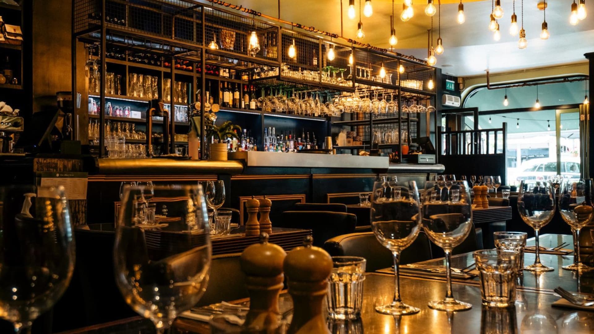 Wine glasses on a table with the bar glowing behind