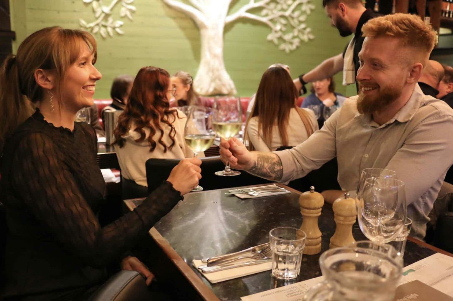 Two guests laughing as they clink glasses across the table at The Olive Tree